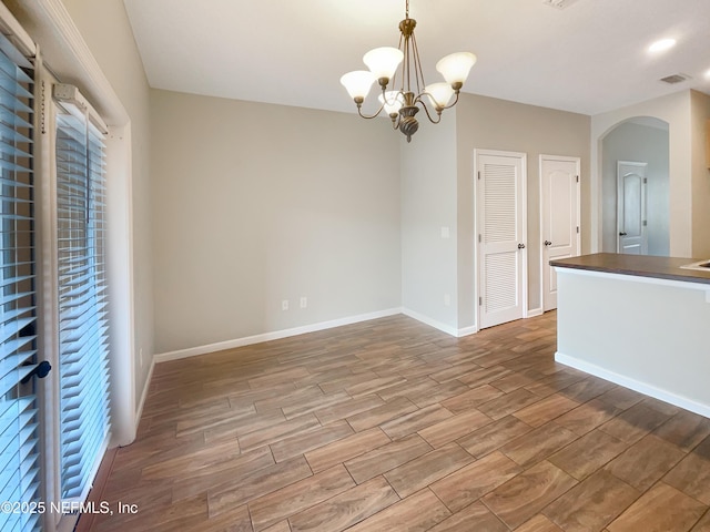 spare room featuring arched walkways, wood finished floors, a chandelier, and baseboards