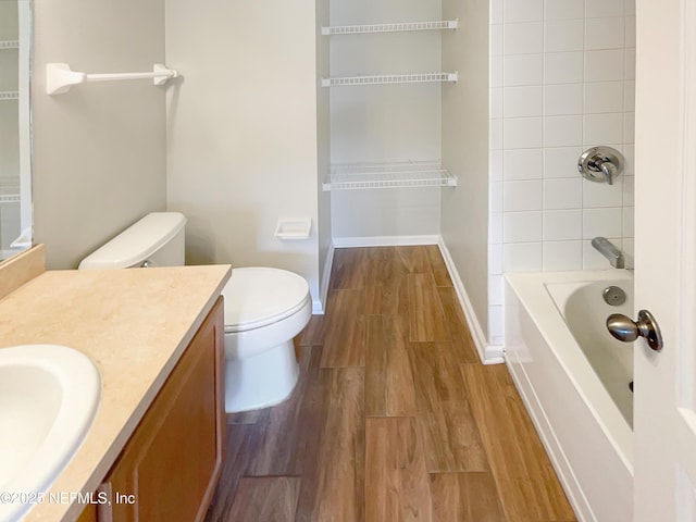 bathroom with baseboards, toilet, wood finished floors, vanity, and bathtub / shower combination