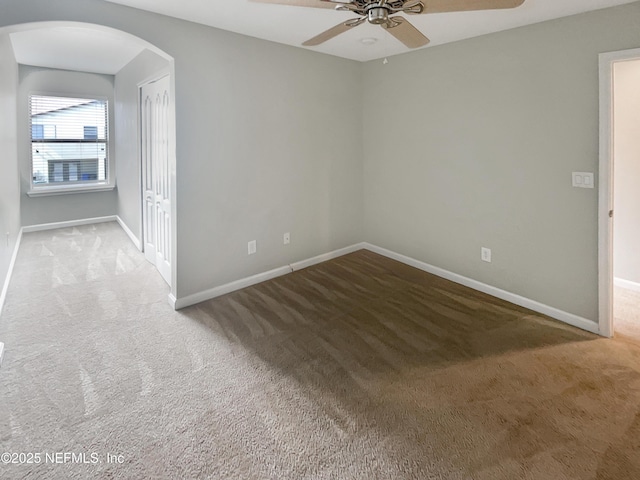 carpeted empty room featuring arched walkways, ceiling fan, and baseboards