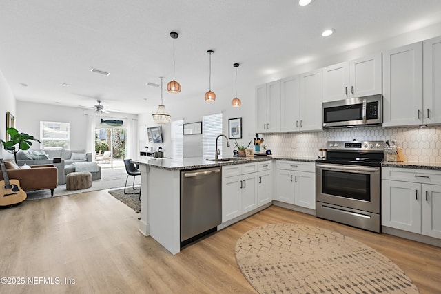 kitchen with a sink, dark stone counters, stainless steel appliances, a peninsula, and tasteful backsplash