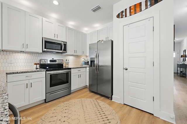 kitchen featuring light stone countertops, appliances with stainless steel finishes, light wood-style floors, decorative backsplash, and visible vents