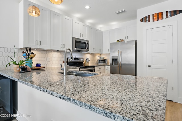 kitchen featuring visible vents, a peninsula, light stone countertops, a sink, and appliances with stainless steel finishes