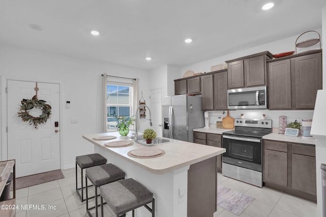 kitchen with stainless steel appliances, light countertops, a sink, light tile patterned flooring, and a center island with sink