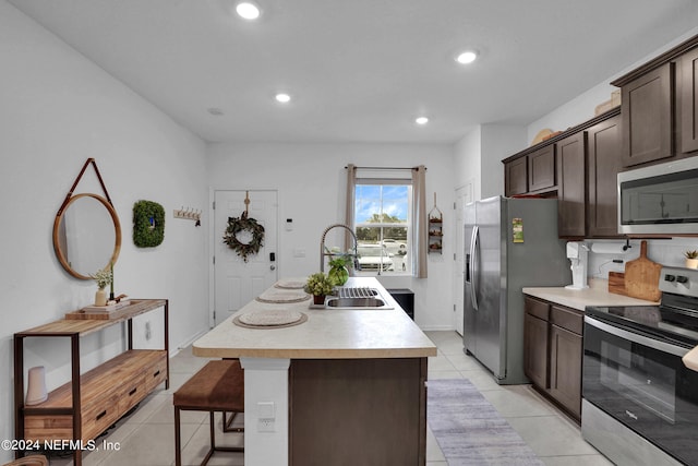 kitchen featuring appliances with stainless steel finishes, light countertops, dark brown cabinets, a sink, and a center island