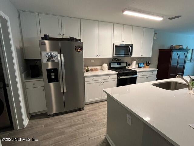 kitchen featuring appliances with stainless steel finishes, a sink, light wood finished floors, white cabinetry, and visible vents