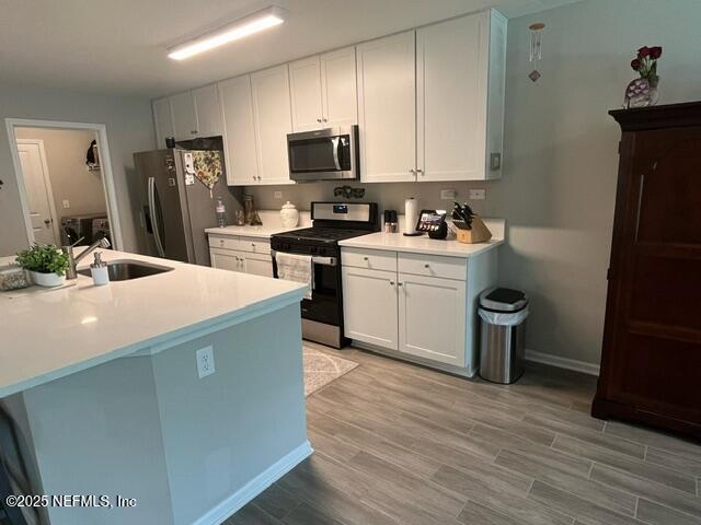 kitchen featuring light wood-type flooring, light countertops, white cabinetry, a sink, and stainless steel appliances
