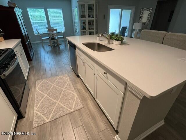 kitchen with a sink, light wood-style floors, dishwasher, range, and white cabinetry