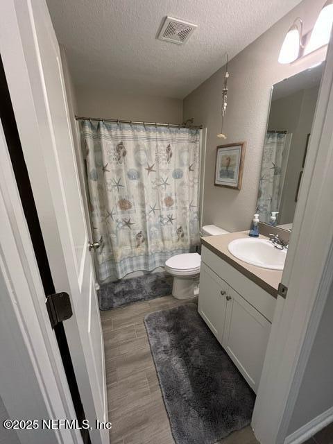 bathroom featuring visible vents, vanity, wood finished floors, toilet, and a textured ceiling