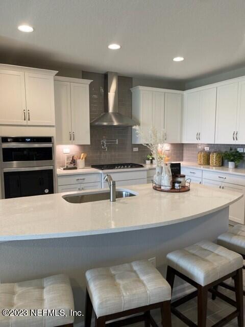 kitchen featuring stainless steel double oven, wall chimney exhaust hood, light countertops, and a sink