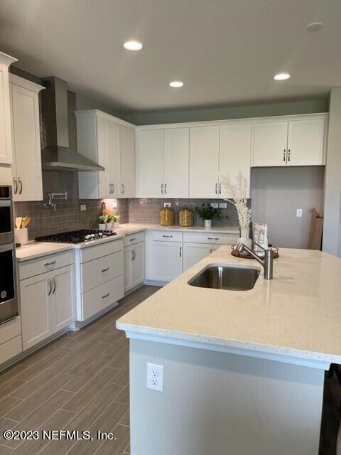 kitchen featuring wall chimney range hood, white cabinetry, tasteful backsplash, a sink, and gas stovetop