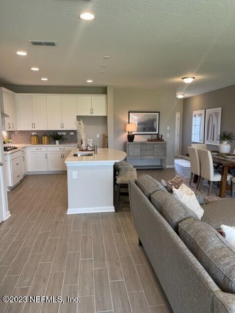 kitchen featuring a kitchen island with sink, decorative backsplash, light countertops, white cabinets, and open floor plan