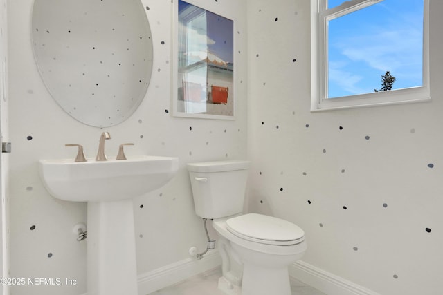 half bathroom with toilet, marble finish floor, a healthy amount of sunlight, and baseboards