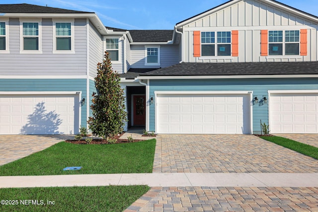 view of property featuring decorative driveway, board and batten siding, a front lawn, and a garage