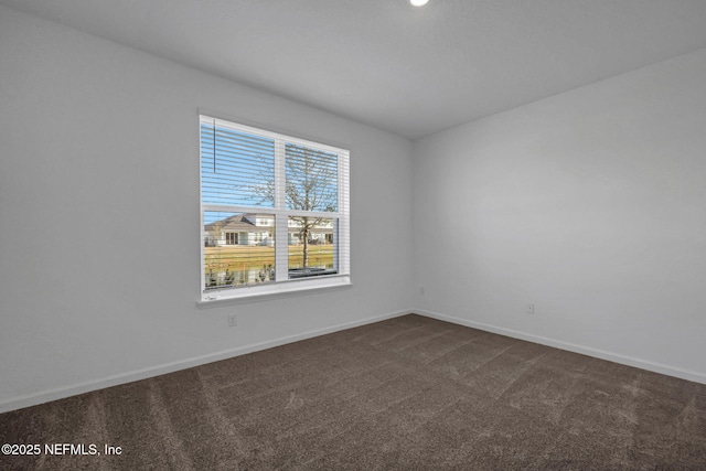 spare room featuring dark carpet and baseboards