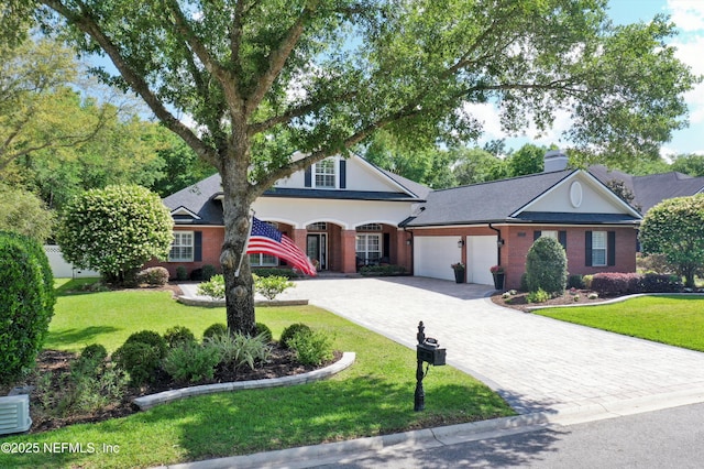traditional-style home with an attached garage, a front yard, decorative driveway, and brick siding