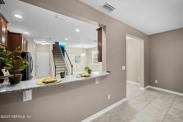 133 San Briso Way, Saint Augustine, FL 32092 - kitchen featuring freestanding refrigerator, a peninsula, light stone counters, a breakfast bar area, and light tile patterned floors