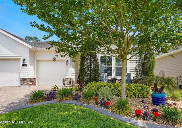 view of property hidden behind natural elements with decorative driveway, an attached garage, and stone siding