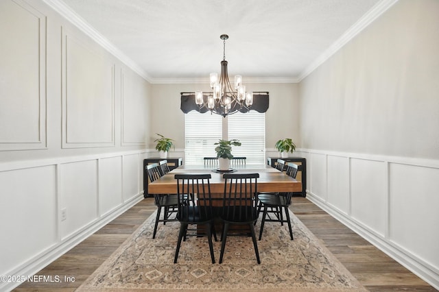 dining room with crown molding, an inviting chandelier, wood finished floors, and a decorative wall