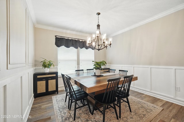 dining room featuring crown molding, a notable chandelier, a decorative wall, a wainscoted wall, and wood finished floors