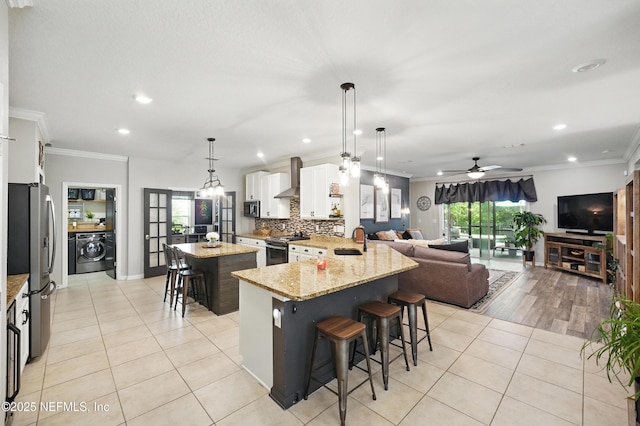 kitchen with wall chimney range hood, a kitchen breakfast bar, washer / dryer, stainless steel appliances, and recessed lighting