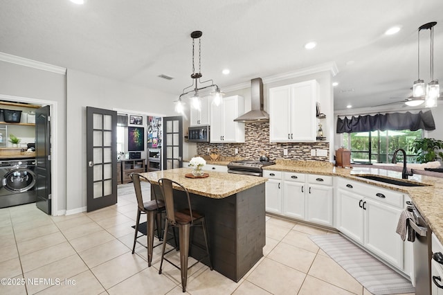 kitchen featuring ornamental molding, washer / clothes dryer, wall chimney exhaust hood, a sink, and appliances with stainless steel finishes