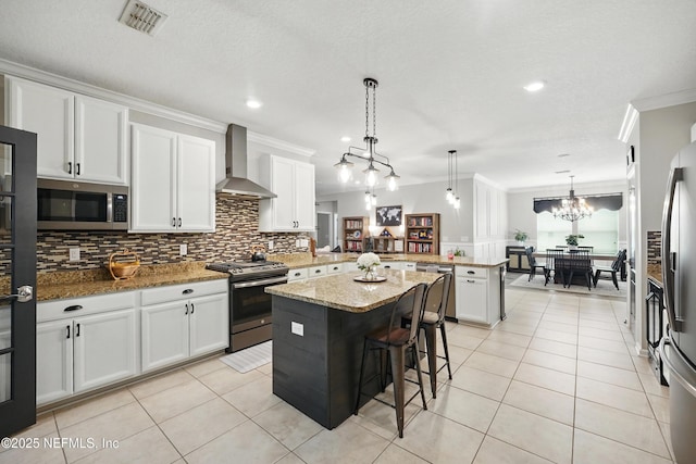 kitchen with wall chimney range hood, visible vents, a peninsula, ornamental molding, and stainless steel appliances