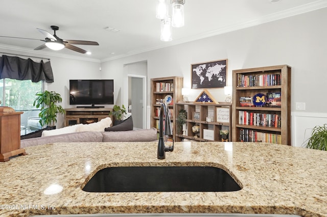 kitchen featuring a ceiling fan, light stone counters, ornamental molding, and a sink