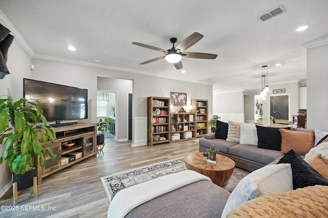 living area featuring ceiling fan, visible vents, crown molding, light wood-type flooring, and recessed lighting