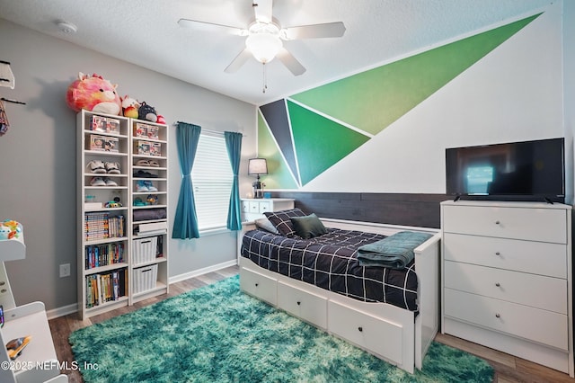 bedroom with a textured ceiling, baseboards, a ceiling fan, and wood finished floors