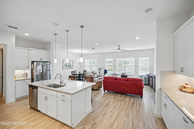 kitchen with white cabinets, appliances with stainless steel finishes, a sink, light wood-style flooring, and decorative backsplash