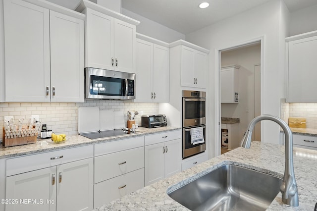 kitchen with a sink, appliances with stainless steel finishes, backsplash, and white cabinets