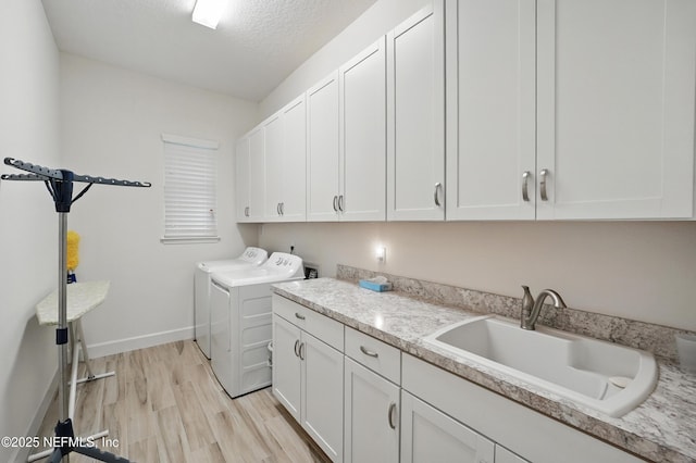 washroom featuring cabinet space, a sink, baseboards, light wood finished floors, and washer and clothes dryer