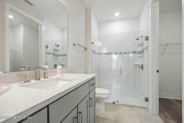 full bathroom featuring a walk in closet, a shower stall, toilet, and vanity