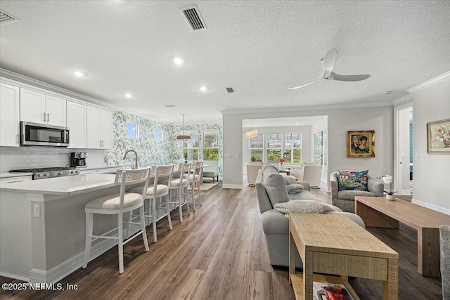 living area with light wood-style flooring, visible vents, ceiling fan, baseboards, and ornamental molding