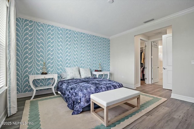 bedroom featuring crown molding, wallpapered walls, wood finished floors, and baseboards
