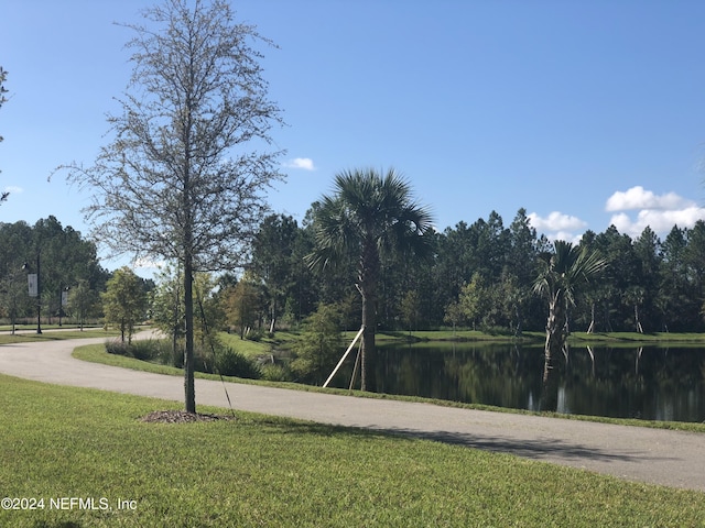 view of property's community featuring a lawn, a water view, and curved driveway