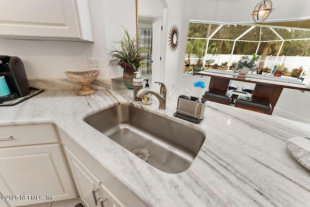room details featuring light stone countertops, a sink, and white cabinetry