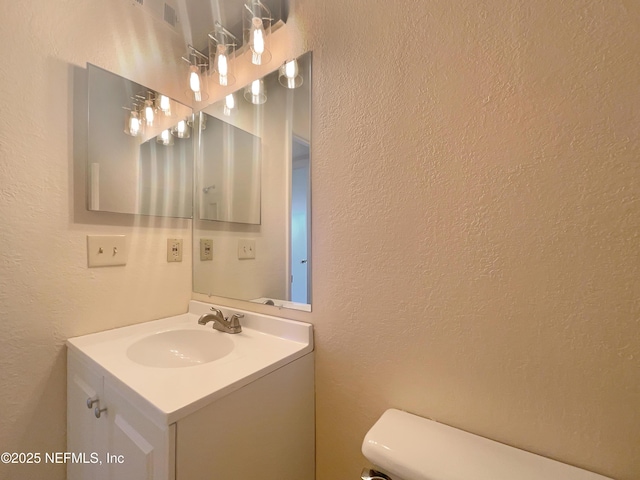 half bathroom with vanity, toilet, and a textured wall