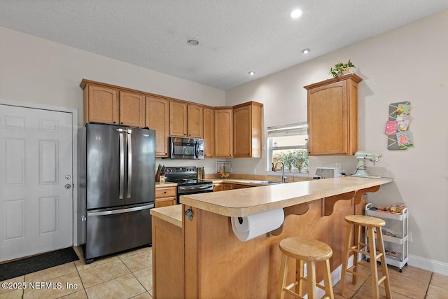 kitchen with a peninsula, light tile patterned flooring, a kitchen bar, light countertops, and stainless steel appliances