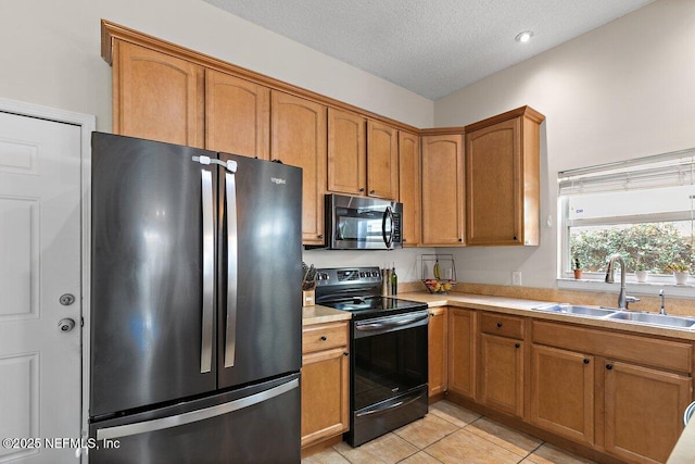 kitchen with light countertops, a textured ceiling, a sink, appliances with stainless steel finishes, and light tile patterned floors