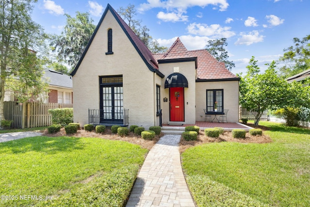 view of front of home with a front lawn, stucco siding, french doors, and fence