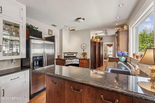 kitchen featuring appliances with stainless steel finishes, a sink, light wood finished floors, dark stone countertops, and visible vents