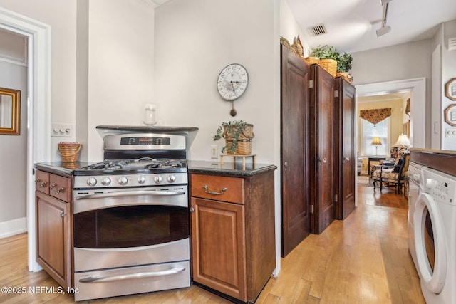 kitchen with light wood finished floors, stainless steel gas stove, brown cabinetry, washer / clothes dryer, and visible vents