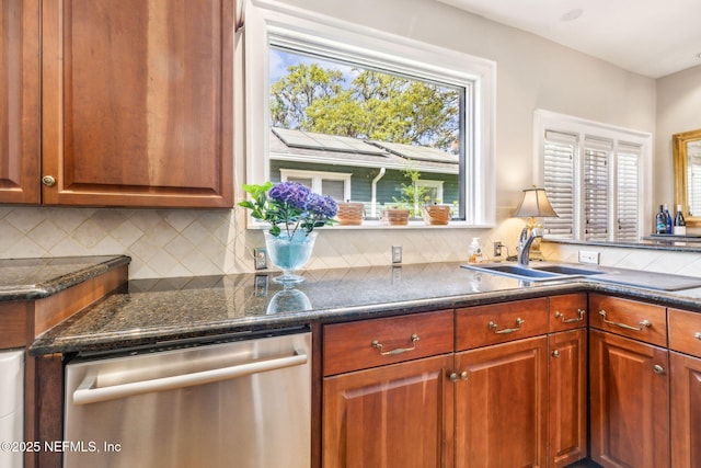 kitchen featuring a sink, dishwasher, brown cabinetry, dark stone countertops, and decorative backsplash