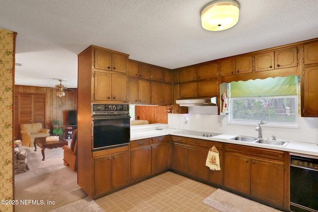 kitchen with under cabinet range hood, light countertops, brown cabinets, black appliances, and a sink