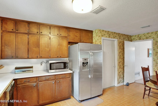 kitchen featuring wallpapered walls, stainless steel appliances, light countertops, brown cabinets, and visible vents