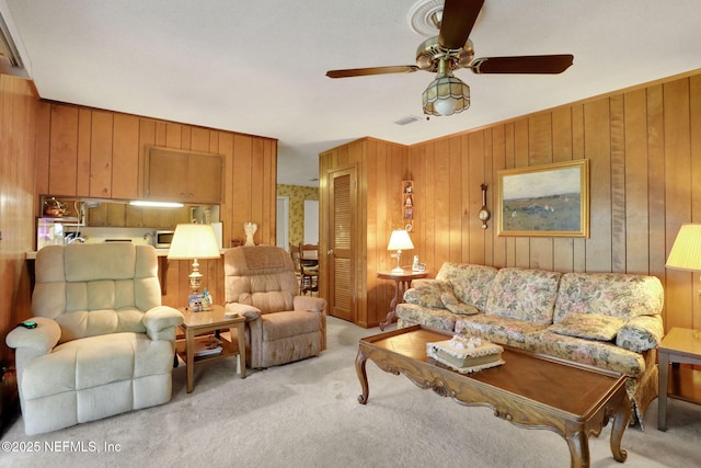 living room featuring wood walls, light colored carpet, ceiling fan, and visible vents