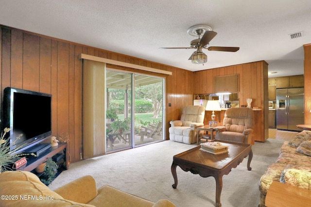 living area with visible vents, ceiling fan, wooden walls, and light colored carpet