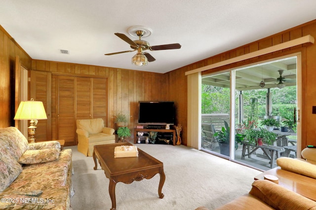 living area with wood walls, carpet, visible vents, and a ceiling fan