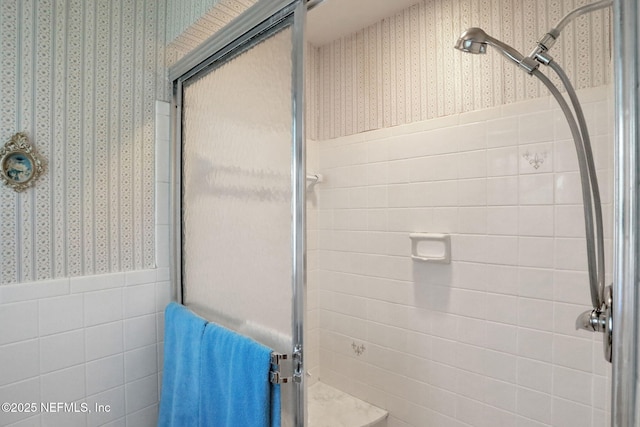 bathroom featuring a shower stall, tile walls, wallpapered walls, and wainscoting